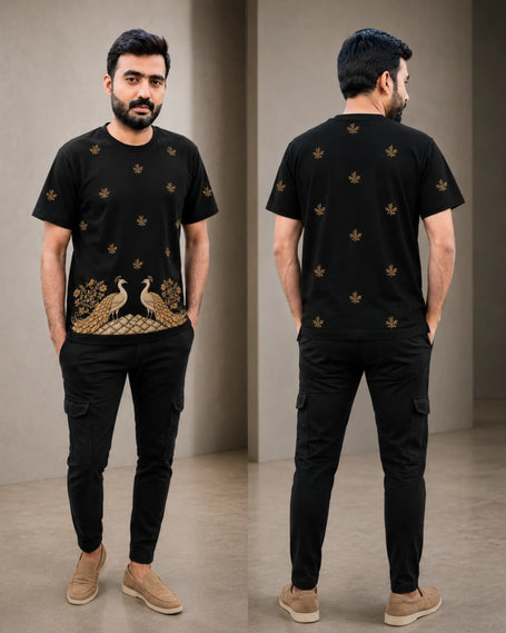 A man modeling a black short-sleeve t-shirt with gold peacock and floral embroidery, shown in front and back views against a neutral indoor backdrop.