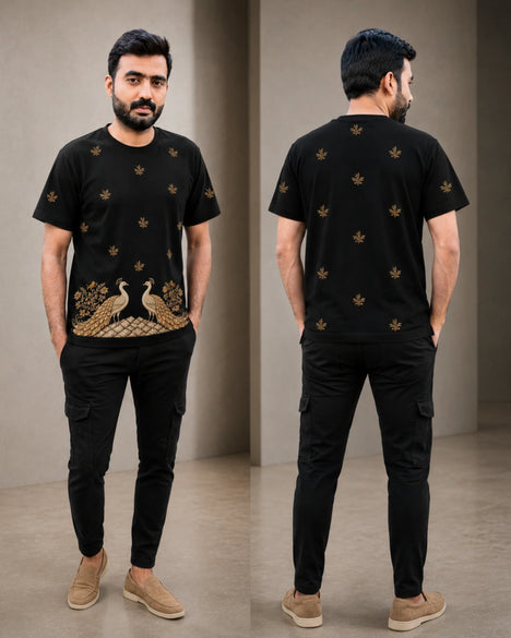 A man modeling a black short-sleeve t-shirt with gold peacock and floral embroidery, shown in front and back views against a neutral indoor backdrop.