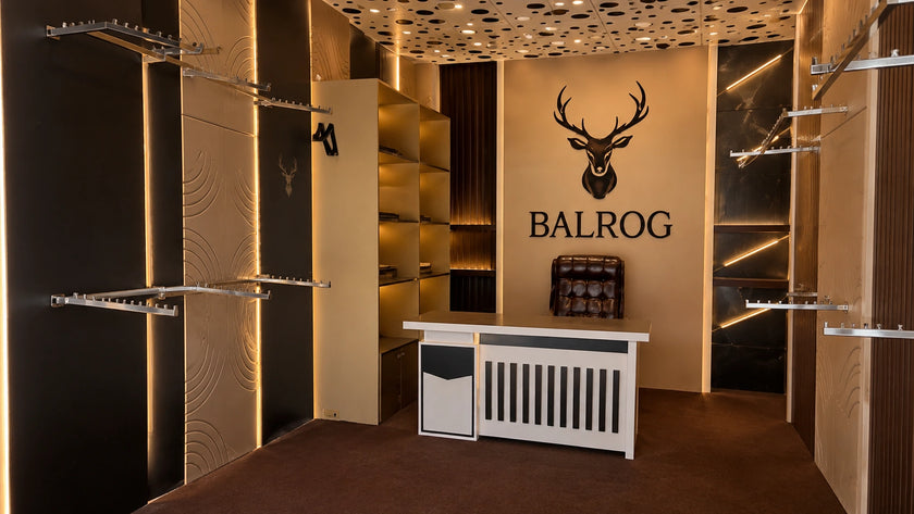 A luxury retail showroom interior featuring the BALROG brand name and deer head logo on a beige wall, with shelving, clothing racks, and a white counter in a modern warm-toned boutique.