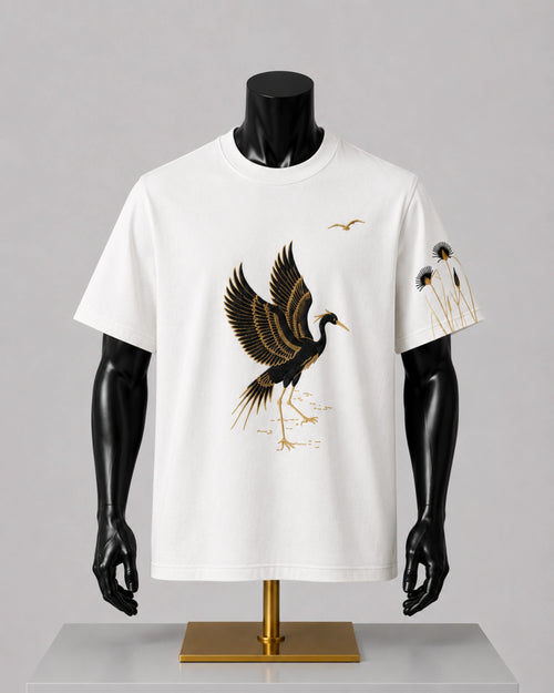 A white short-sleeve t-shirt displayed on a black mannequin torso with a gold stand, featuring a large black and gold crane graphic on the front and smaller crane and floral prints on the sleeve.
