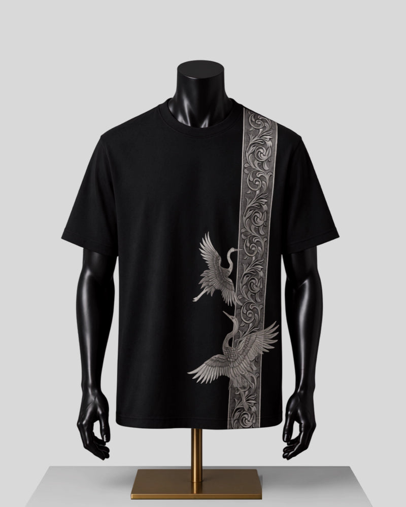 A black short-sleeve t-shirt displayed on a black mannequin torso with a gold stand, featuring a vertical silver-gray ornate patterned stripe down the right side and a large silver crane graphic on the front.