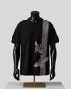 A black short-sleeve t-shirt displayed on a black mannequin torso with a gold stand, featuring a vertical silver-gray ornate patterned stripe down the right side and a large silver crane graphic on the front.