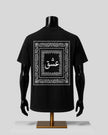 A black short-sleeve T-shirt displayed on a black mannequin torso with arms and a stand, shown from the back. The shirt features a large white ornate border graphic with Arabic calligraphy in the center.