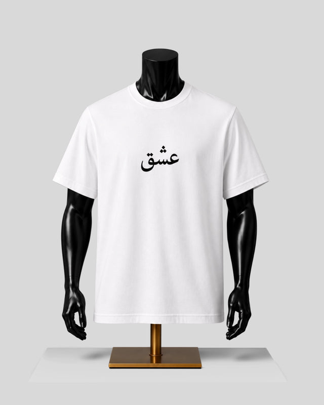 A white short-sleeve crewneck T-shirt displayed on a black mannequin torso with a gold stand against a light gray background. The shirt features black Arabic calligraphy printed on the center chest.
