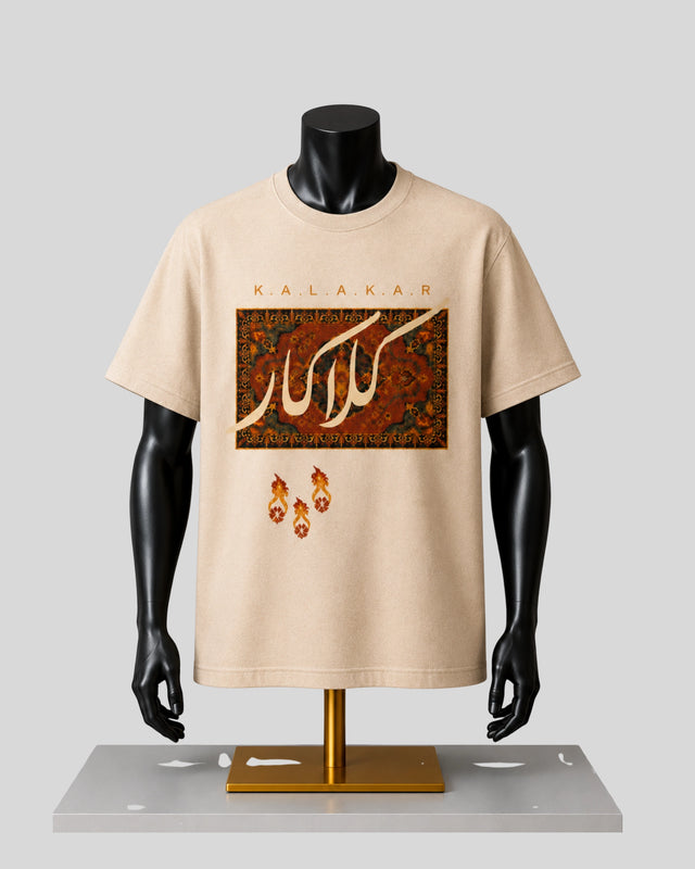 A beige short-sleeve graphic T-shirt displayed on a black mannequin torso with a gold stand against a light gray background. The shirt features the word 'KALAKAR' above a rectangular ornate pattern in red, gold, and brown, with three small flame-like motifs below.
