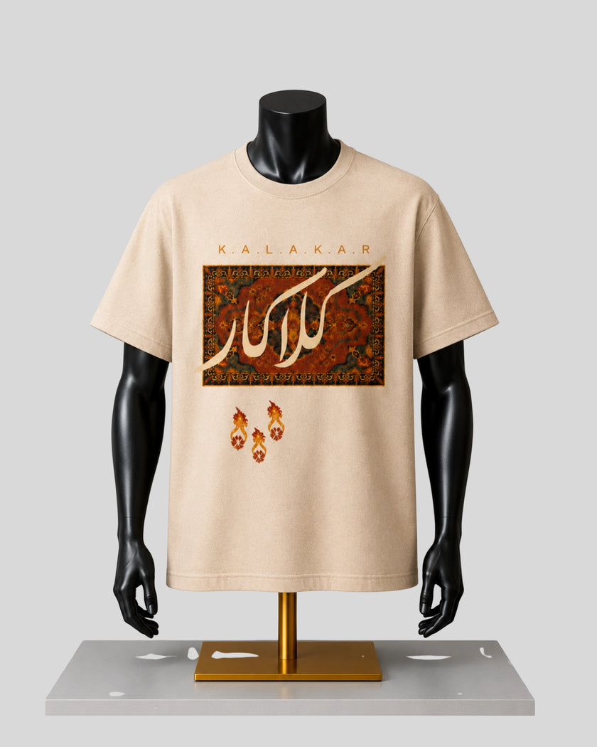 A beige short-sleeve graphic T-shirt displayed on a black mannequin torso with a gold stand against a light gray background. The shirt features the word 'KALAKAR' above a rectangular ornate pattern in red, gold, and brown, with three small flame-like motifs below.