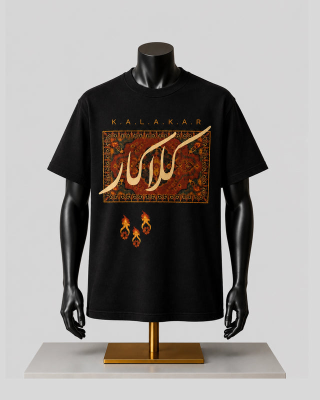 A black short-sleeve graphic T-shirt displayed on a black mannequin torso with arms and hands, standing on a gold-colored stand against a light gray background. The shirt features a large rectangular graphic with Arabic calligraphy in gold over a red and brown patterned design, with the text 'K.