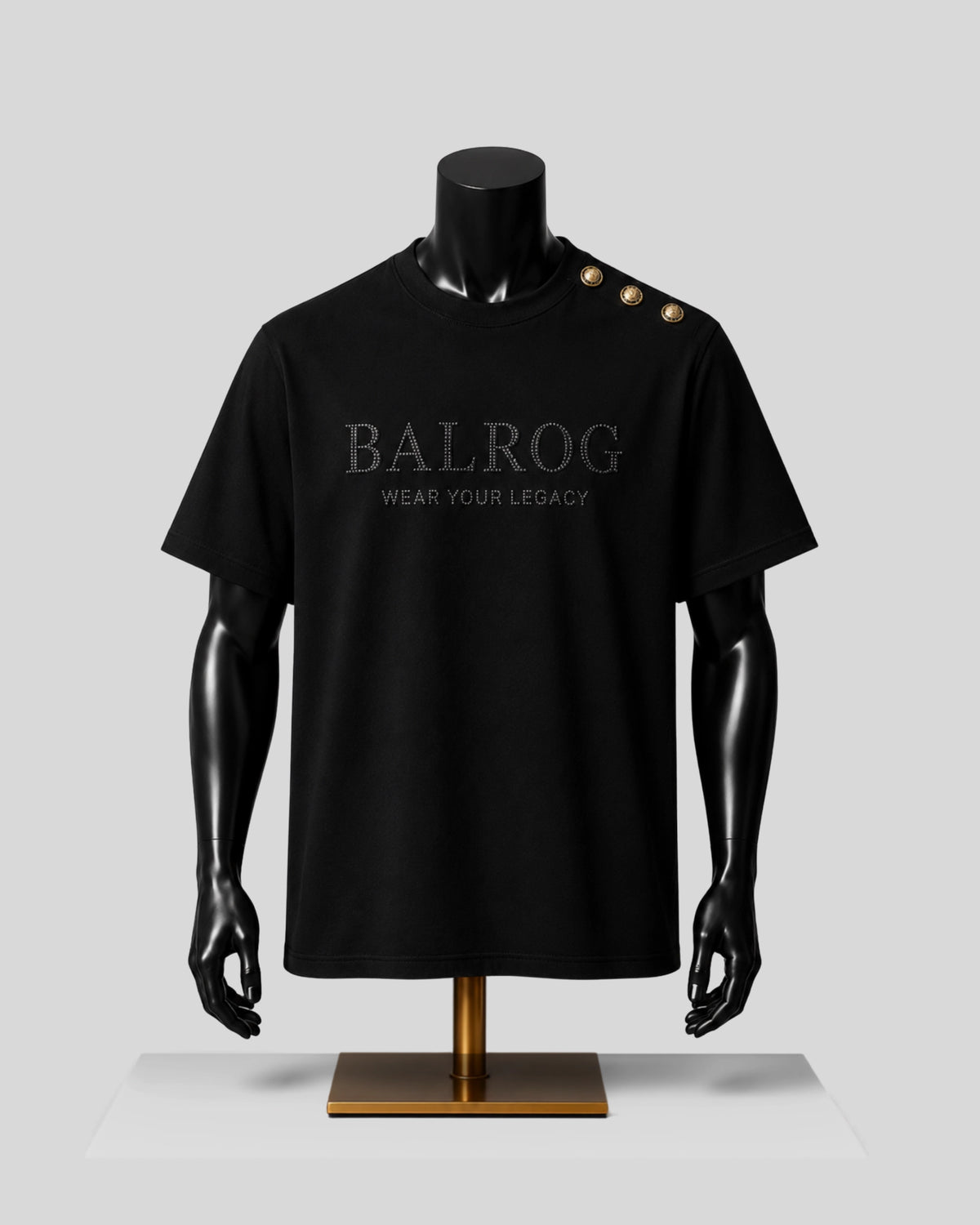 A black Balrog short-sleeve t-shirt displayed on a black mannequin torso with a gold stand, featuring 'BALROG WEAR YOUR LEGACY' printed on the chest and three gold buttons on the shoulder.