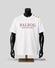 A white short-sleeve T-shirt displayed on a black mannequin torso with gold buttons on the shoulder. The front has the text 'BALROG' in burgundy with 'WEAR YOUR LEGACY' underneath.