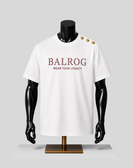 A white short-sleeve T-shirt displayed on a black mannequin torso with gold buttons on the shoulder. The front has the text 'BALROG' in burgundy with 'WEAR YOUR LEGACY' underneath.