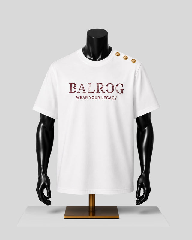 A white short-sleeve T-shirt displayed on a black mannequin torso with gold buttons on the shoulder. The front has the text 'BALROG' in burgundy with 'WEAR YOUR LEGACY' underneath.