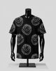 A black short-sleeve t-shirt with a white dotted rose pattern, displayed on a black mannequin torso against a light gray background.