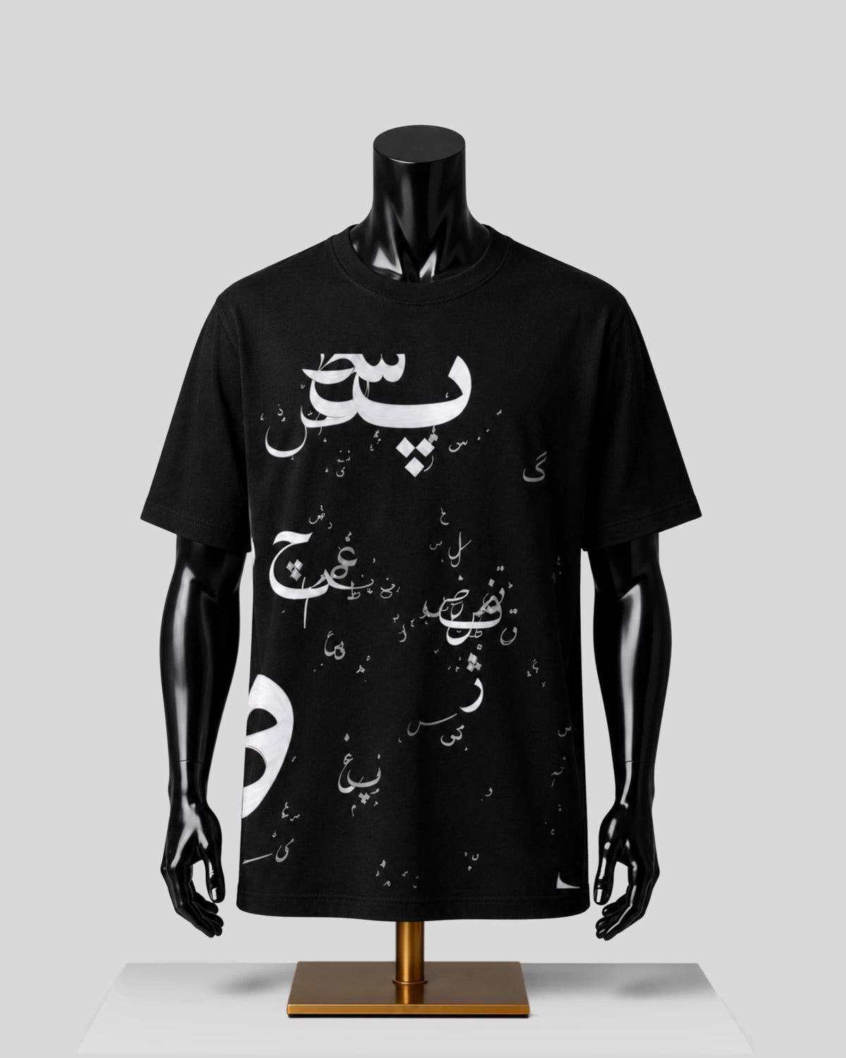 A black short-sleeve t-shirt with white Arabic calligraphy printed on the front, displayed on a black mannequin torso with a gold stand against a light gray background.