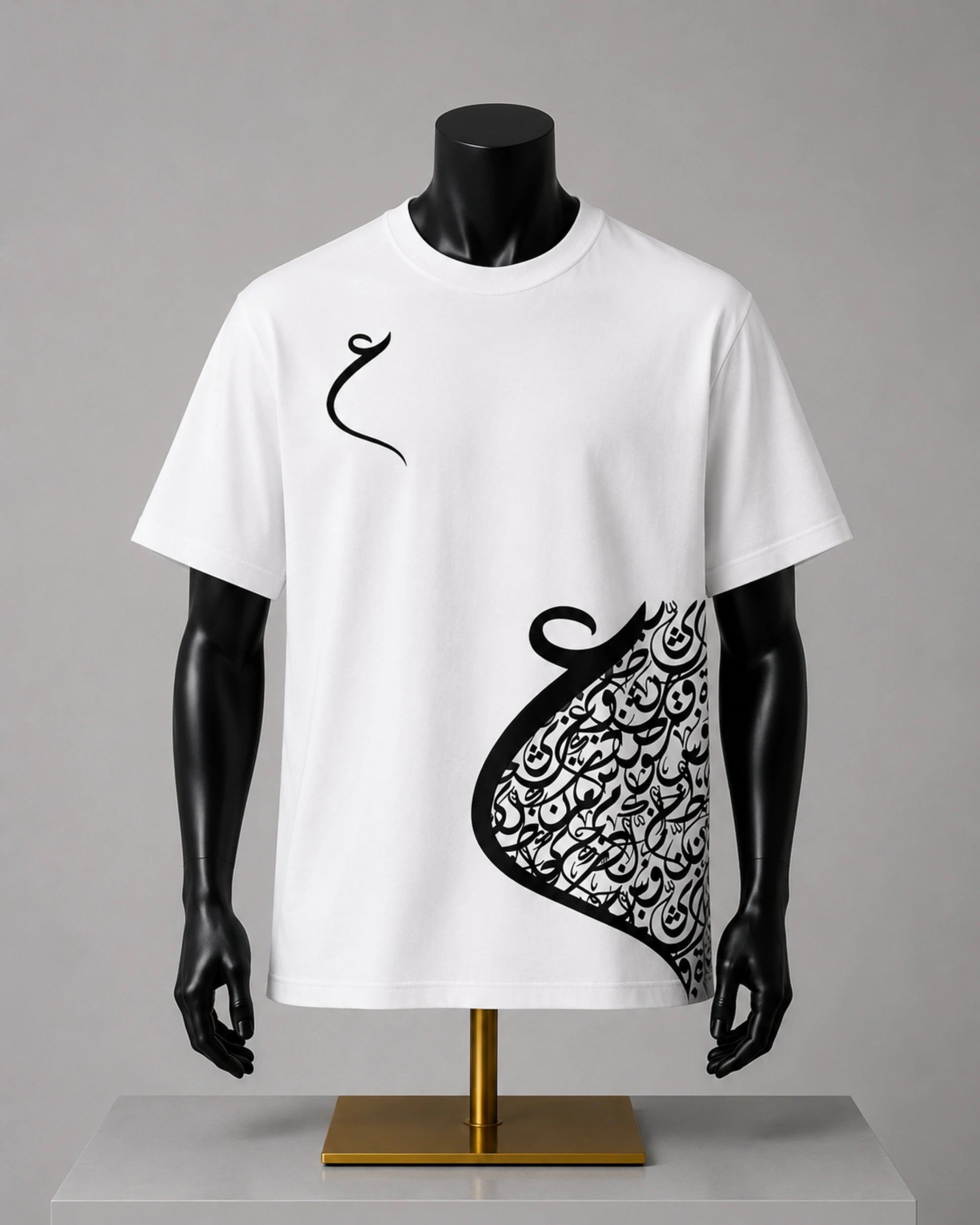 A white short-sleeve t-shirt displayed on a black mannequin torso with a gold stand against a neutral gray background. The shirt features a black Arabic calligraphy graphic, resembling a stylized crescent or abstract scroll, printed on the right side and a small matching calligraphy motif on the left chest.