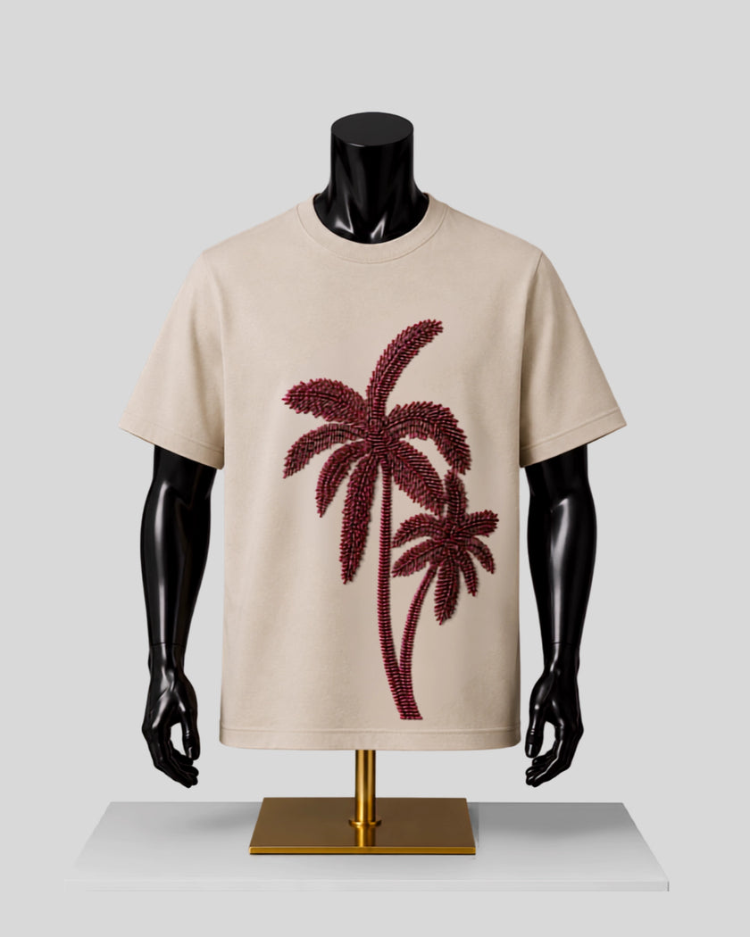 A beige short-sleeve crewneck T-shirt displayed on a black mannequin torso with a gold stand, featuring a large dark red palm tree graphic on the front.
