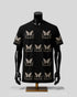A black short-sleeve t-shirt with a repeating beige butterfly and floral pattern, displayed on a black mannequin torso with a gold stand against a light gray background.