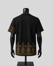 Black short-sleeve t-shirt displayed on a black mannequin from the back, featuring ornate gold patterns along the lower hem and one sleeve, against a light gray background.