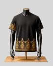 A black short-sleeve t-shirt with intricate gold geometric and tribal-style embroidery, displayed on a black mannequin torso over a light wood stand against a solid gray background.