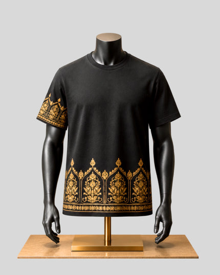 A black short-sleeve t-shirt with intricate gold geometric and tribal-style embroidery, displayed on a black mannequin torso over a light wood stand against a solid gray background.