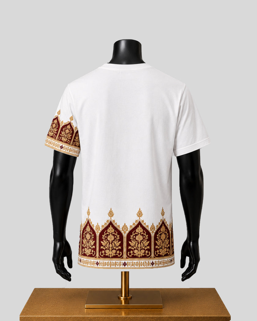 White short-sleeve t-shirt shown from the back on a black mannequin torso, featuring ornate gold and dark red embroidered arch motifs along the bottom hem and left sleeve, displayed on a wooden stand against a light gray background.