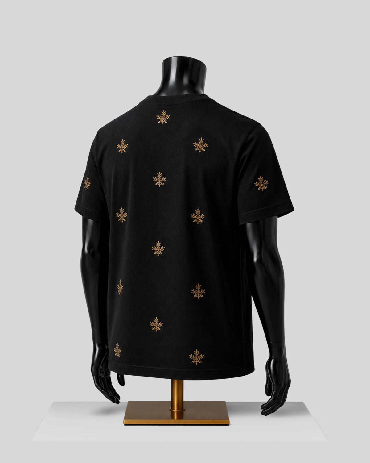 A black short-sleeve T-shirt displayed on a black mannequin torso with a gold stand, featuring a scattered gold fleur-de-lis pattern on the back, set against a light gray background.