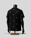 A black short-sleeve T-shirt displayed on a black mannequin torso with a gold stand, featuring a scattered gold fleur-de-lis pattern on the back, set against a light gray background.