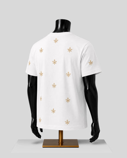 White short-sleeve t-shirt displayed on a black mannequin torso, showing the back view with a scattered gold snowflake pattern, set against a light gray background.