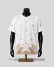 White short-sleeve crewneck T-shirt displayed on a black mannequin torso with a gold embroidered design featuring peacocks and floral motifs, set against a light gray background.