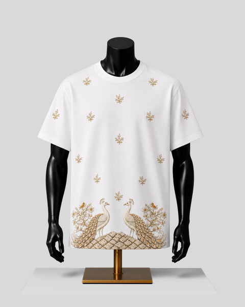 White short-sleeve crewneck T-shirt displayed on a black mannequin torso with a gold embroidered design featuring peacocks and floral motifs, set against a light gray background.