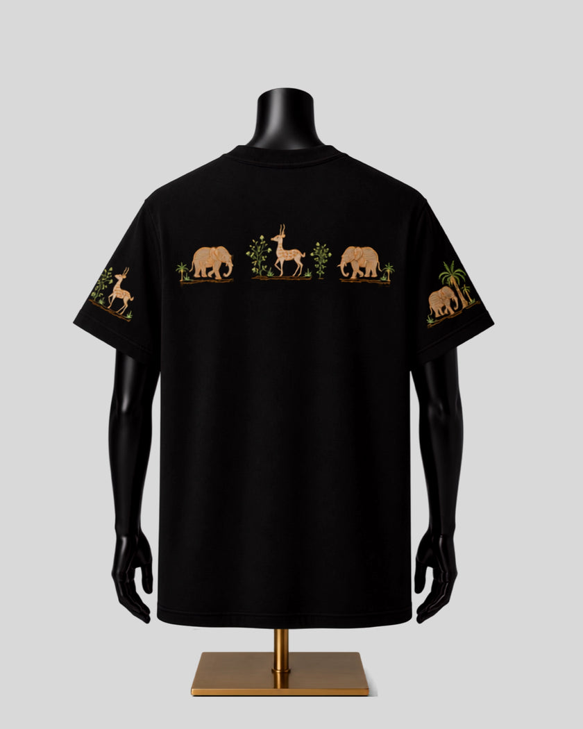 A black short-sleeve T-shirt displayed on a black mannequin torso with a gold stand, featuring a horizontal safari animal print across the chest and sleeve cuffs in tan, green, and brown on a light gray background.
