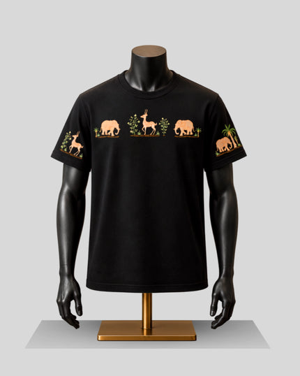 A black short-sleeve crewneck t-shirt displayed on a black mannequin torso with a gold stand. The shirt features a horizontal graphic print across the chest and upper sleeves depicting safari animals, including giraffes, elephants, and palm trees, in tan and green.