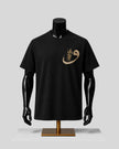 A black short-sleeve crewneck t-shirt displayed on a black mannequin torso with a gold graphic on the left chest, set against a light gray background.