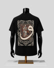 A black short-sleeve T-shirt displayed on a black mannequin torso with a gold stand, shown from the back. The shirt features a large medieval-style illuminated manuscript illustration with a prominent cream-colored snake coiling through the design.