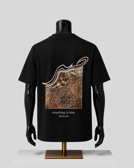 A black short-sleeve T-shirt displayed on a black mannequin torso, showing the back side with a large square graphic print in brown and beige tones. The graphic includes Arabic calligraphy and the text 'everything, in time' and 'THE POLLUR'.