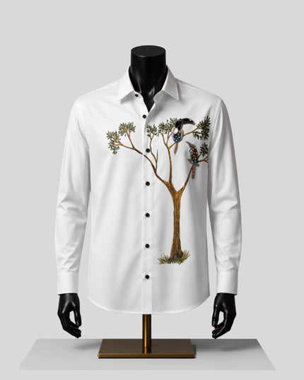 A white long-sleeve button-up shirt displayed on a black mannequin torso with black hands and a gold stand, featuring a large printed graphic of a tree with birds on the front.
