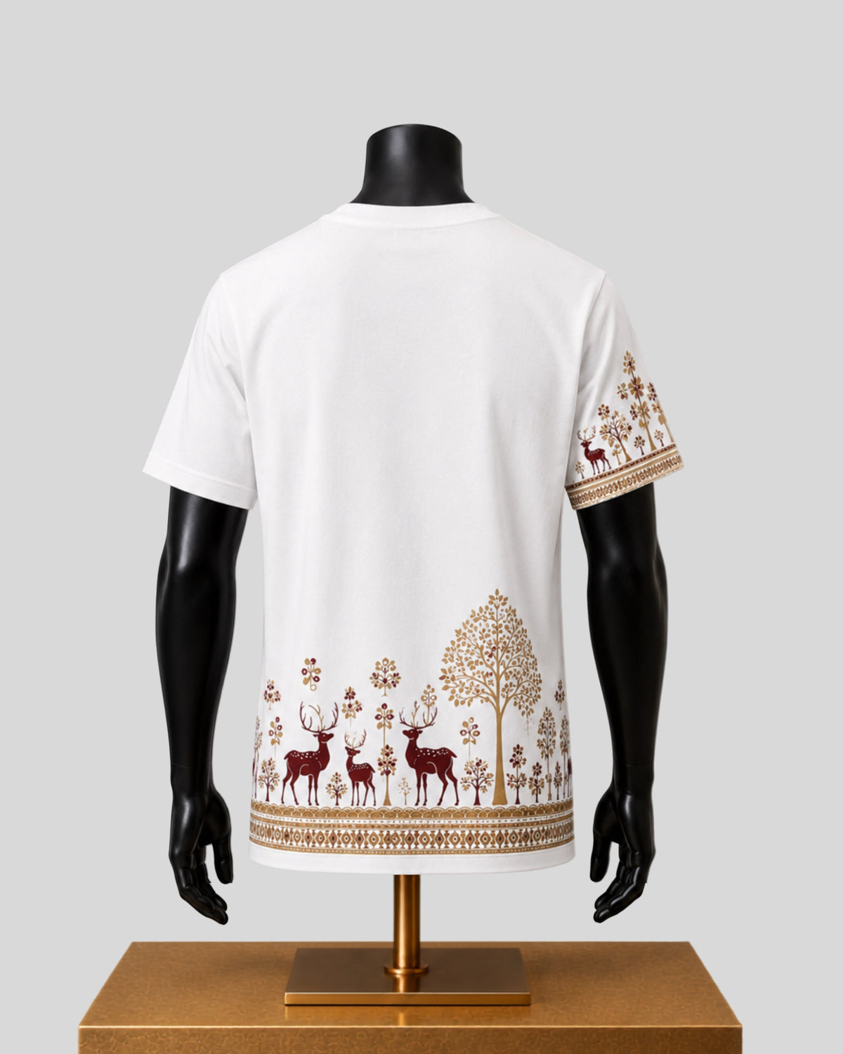 White short-sleeve t-shirt displayed on a black mannequin from the back, featuring a brown forest pattern with deer, trees, and floral motifs along the hem and sleeve.