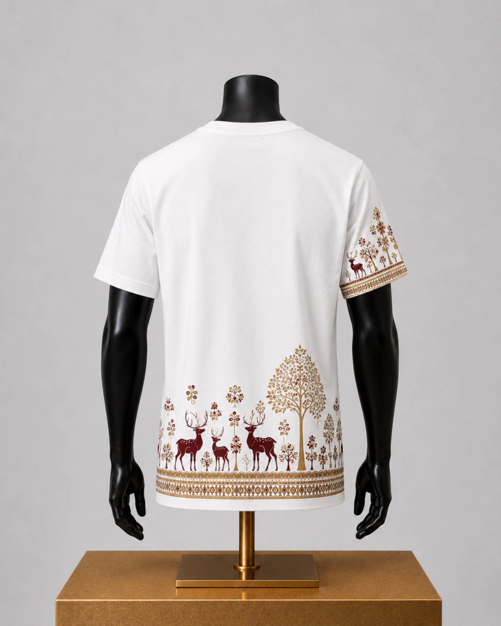 White short-sleeve t-shirt displayed on a black mannequin torso, showing a back view with a forest-themed print of deer, trees, and floral motifs in brown and gold along the hem and sleeve.