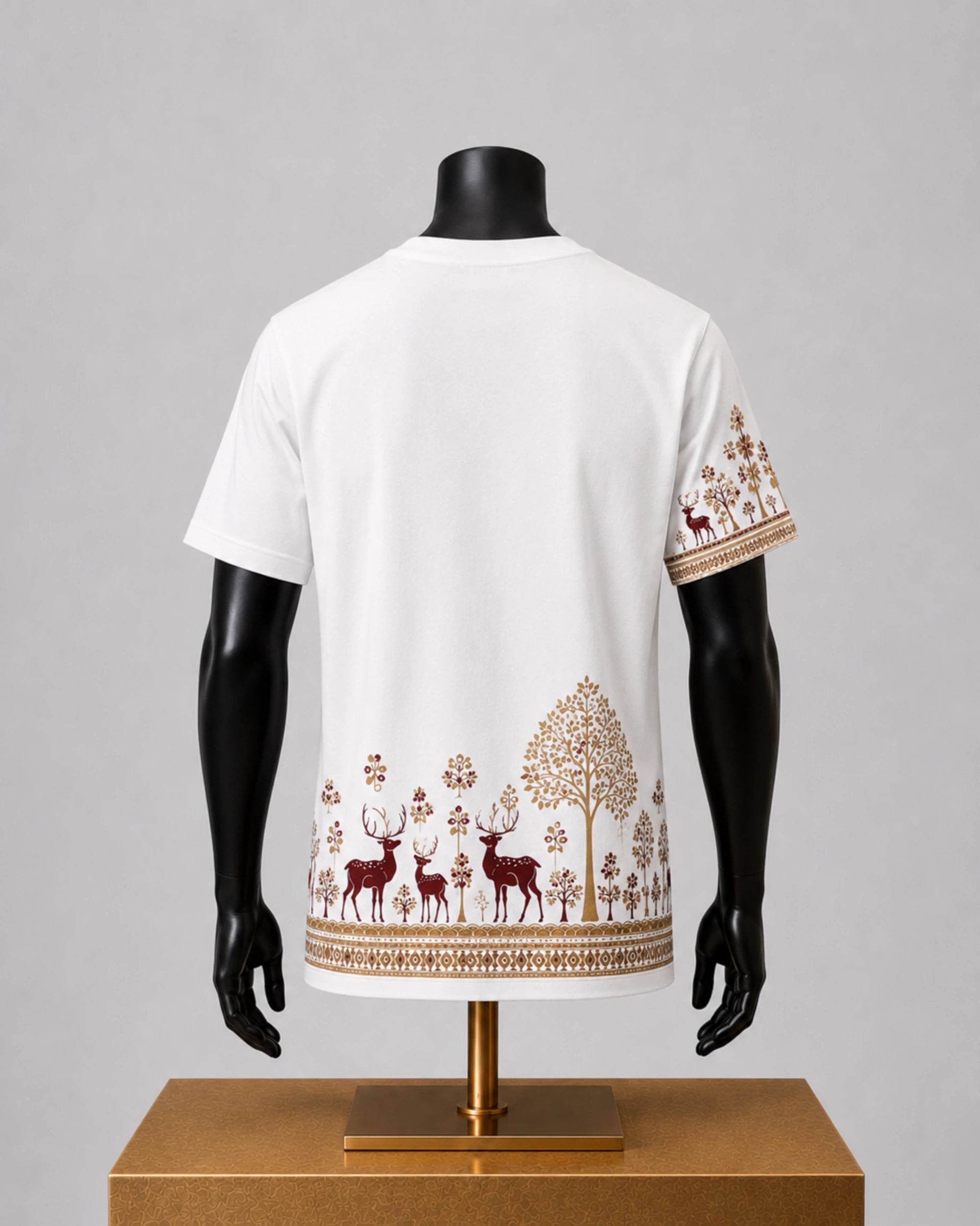 White short-sleeve t-shirt displayed on a black mannequin torso, showing a back view with a forest-themed print of deer, trees, and floral motifs in brown and gold along the hem and sleeve.