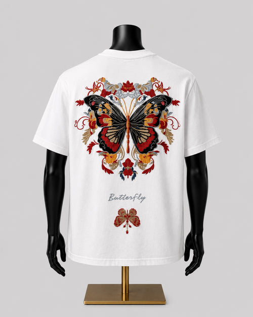 White short-sleeve T-shirt displayed on a black mannequin torso with a gold stand, showing a large butterfly graphic in red, black, and gold tones on the back, with the word 'Butterfly' printed below.