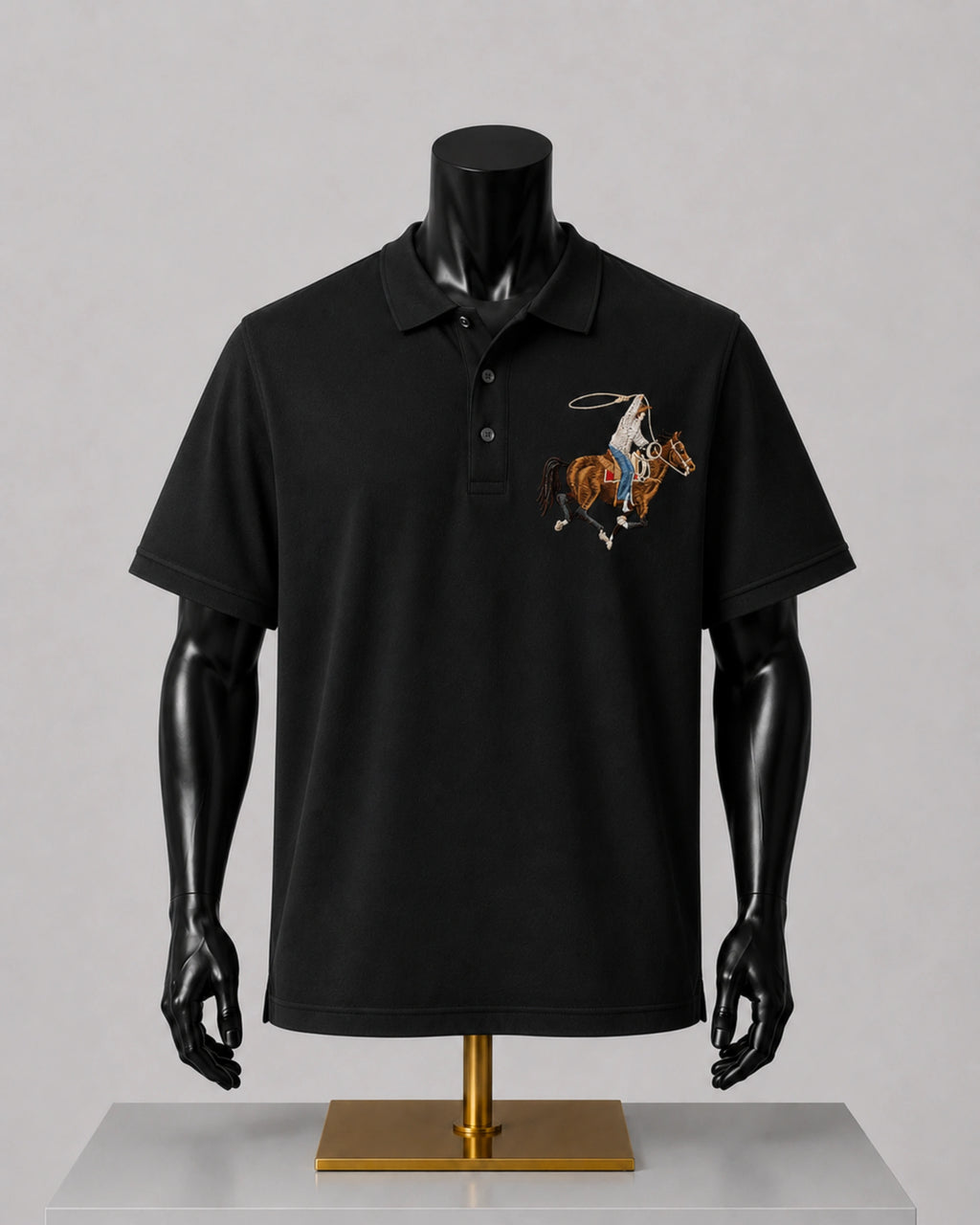 A black short-sleeve polo shirt displayed on a black mannequin torso with a gold stand, featuring a small embroidered cowboy motif on the left chest, set against a neutral gray background.