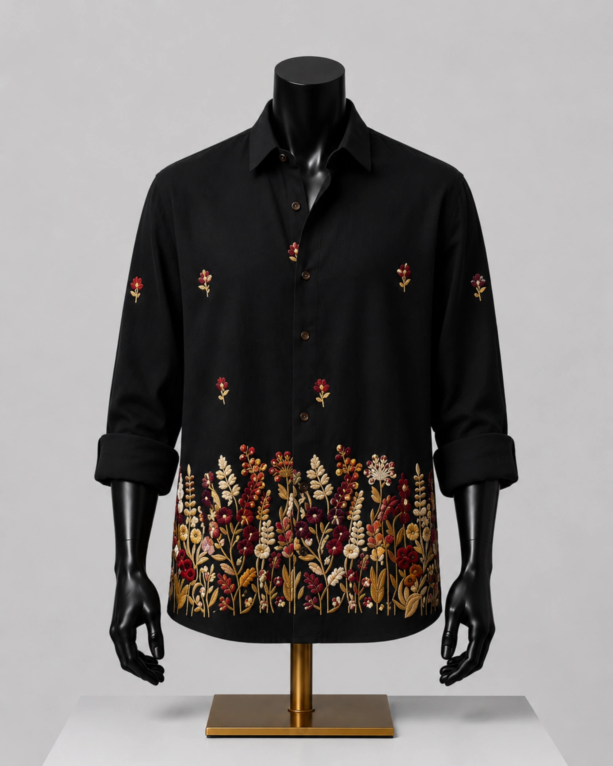 A black long-sleeve button-up shirt displayed on a black mannequin torso with a gold stand, featuring embroidered floral patterns on the front and cuffs, set against a neutral gray background.