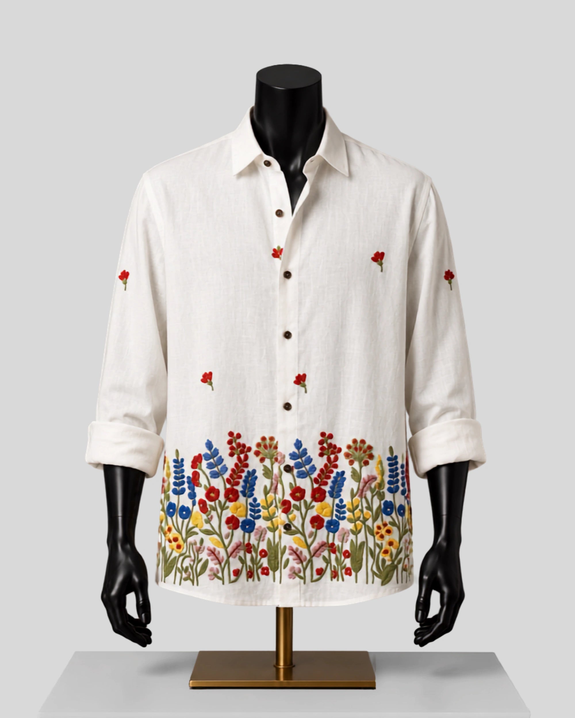 An off-white linen long-sleeve button-up shirt with colorful floral embroidery along the hem and scattered red flower motifs on the sleeves, displayed on a black mannequin torso with a gold stand against a light gray background.