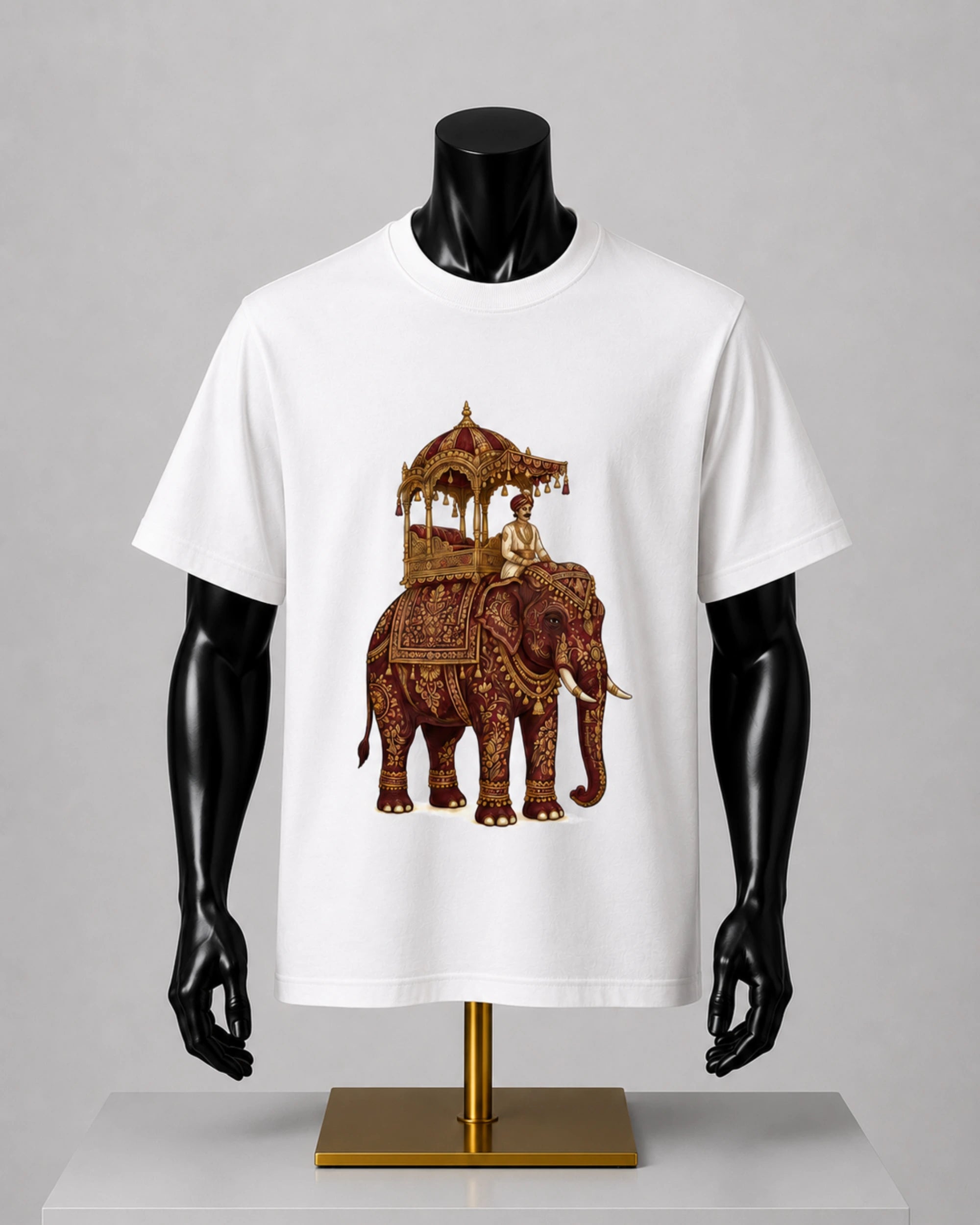 A white short-sleeve crewneck t-shirt displayed on a black mannequin torso. The shirt features a detailed graphic print of an ornate brown and gold decorated elephant carrying a traditional canopy with a rider.