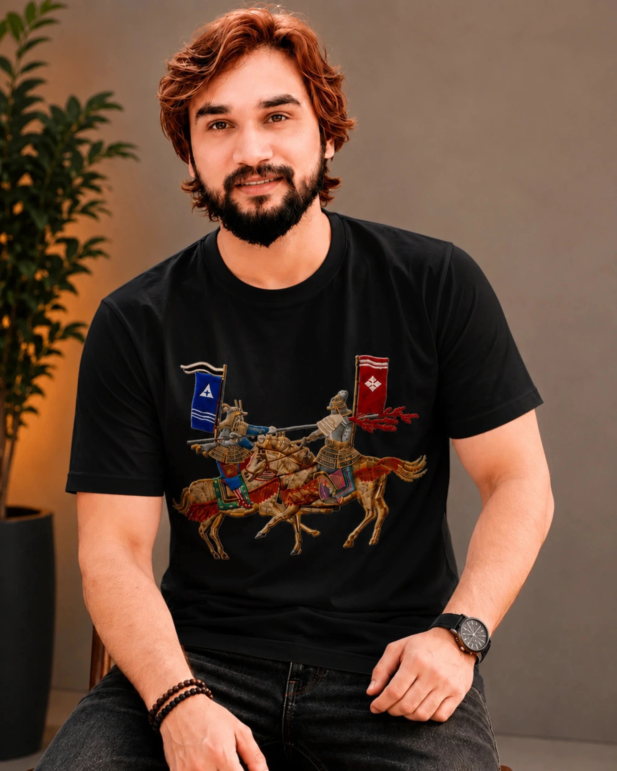 A man wearing a black short-sleeve t-shirt with a detailed graphic of two medieval knights on horseback, posed in an indoor setting with a plant in the background.