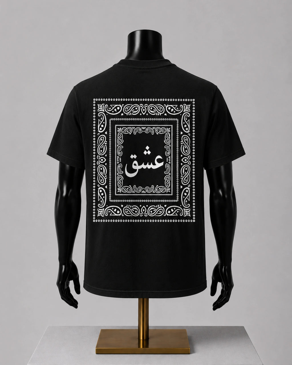 A black short-sleeve T-shirt displayed on a black mannequin torso with arms and a stand, shown from the back. The shirt features a large white ornamental border graphic with Arabic calligraphy in the center.
