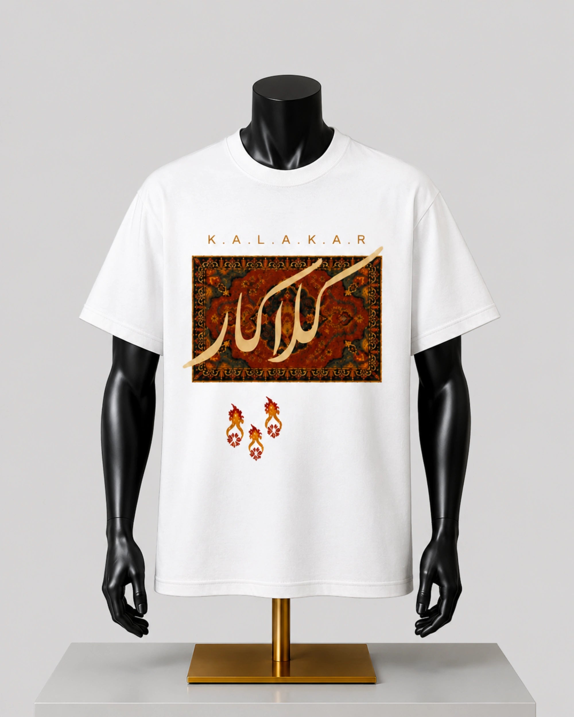 White short-sleeve graphic T-shirt displayed on a black mannequin torso with a gold stand, featuring Arabic calligraphy and the brand name KALAKAR on the front against a light gray background.