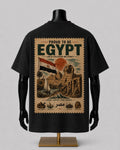 A black short-sleeve T-shirt displayed on a black mannequin torso with a large vintage-style Egypt graphic on the back. The print features the words 'PROUD TO BE EGYPT,' an Egyptian flag, pyramids, the Sphinx, a sailboat, and smaller illustrations along the bottom.