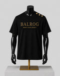 Black short-sleeve Balrog T-shirt displayed on a black mannequin torso with gold lettering on the chest and gold buttons on the shoulder, set against a light gray background.