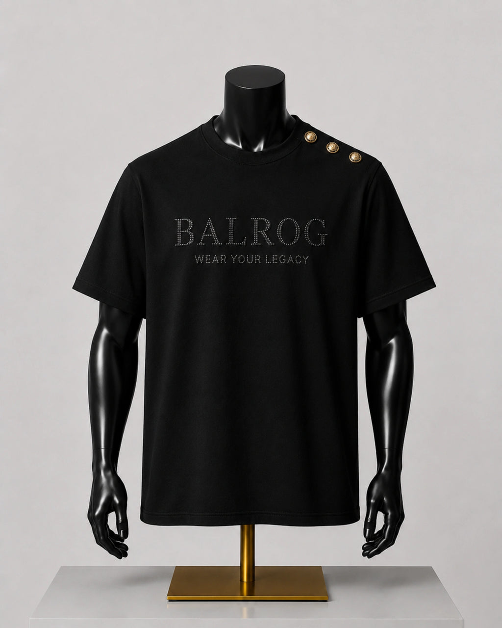 A black short-sleeve Balrog t-shirt displayed on a black mannequin torso with a gold stand, featuring 'BALROG WEAR YOUR LEGACY' printed on the chest and three gold buttons on the shoulder.