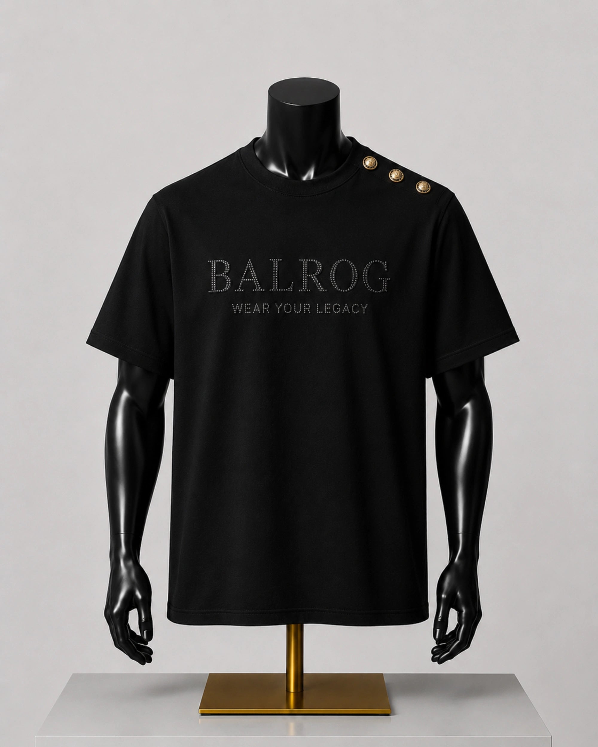 A black short-sleeve Balrog t-shirt displayed on a black mannequin torso with a gold stand, featuring 'BALROG WEAR YOUR LEGACY' printed on the chest and three gold buttons on the shoulder.